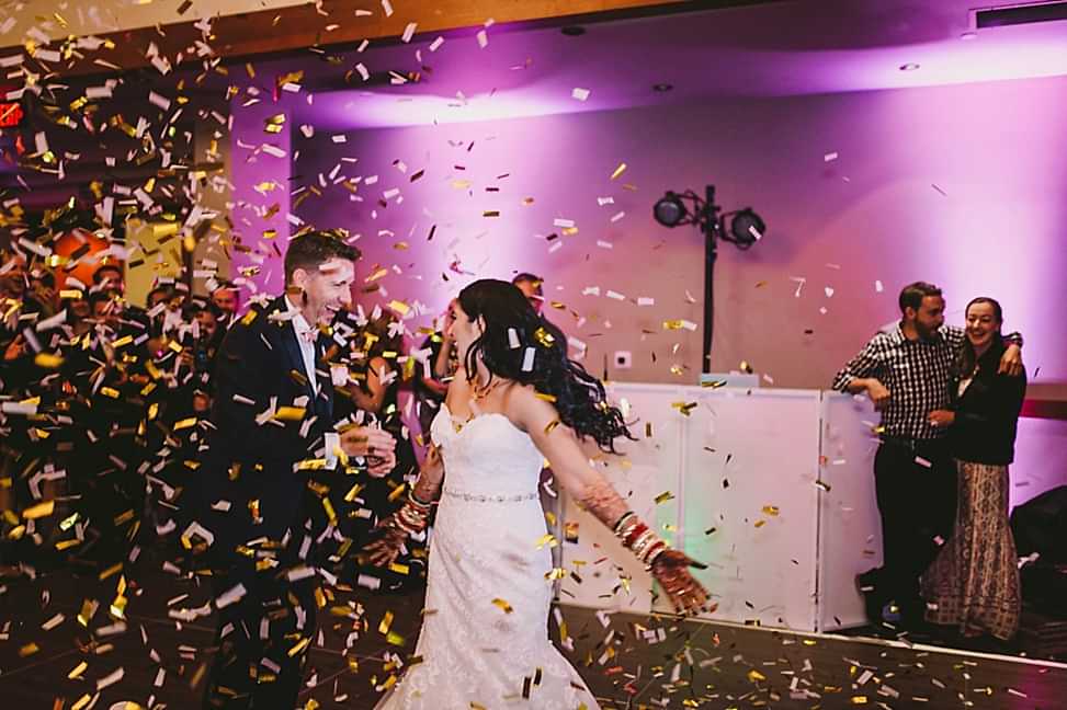 A couple dance on the dance floor as confetti falls from the ceiling during wedding entrance songs.