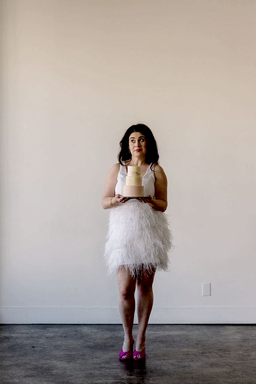 Meg stands and holds a cake.