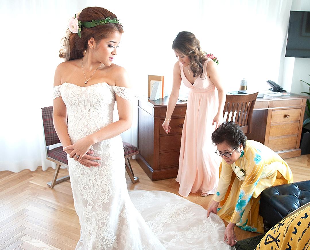A mother helps a bride into her dress.