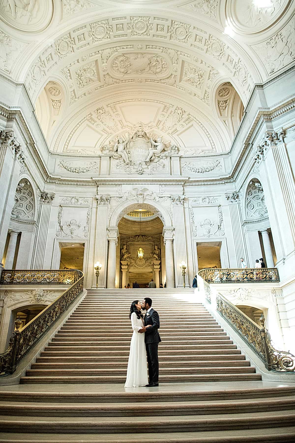 A wedding couple kiss while standing on steps in City Hall