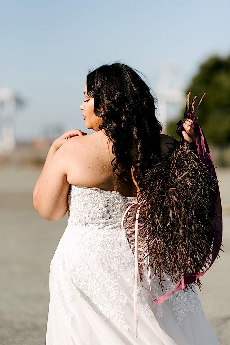 A woman holding a bouquet shows off the corset-style back of the Maggie Sottero wedding dress style 'Vanessa.'