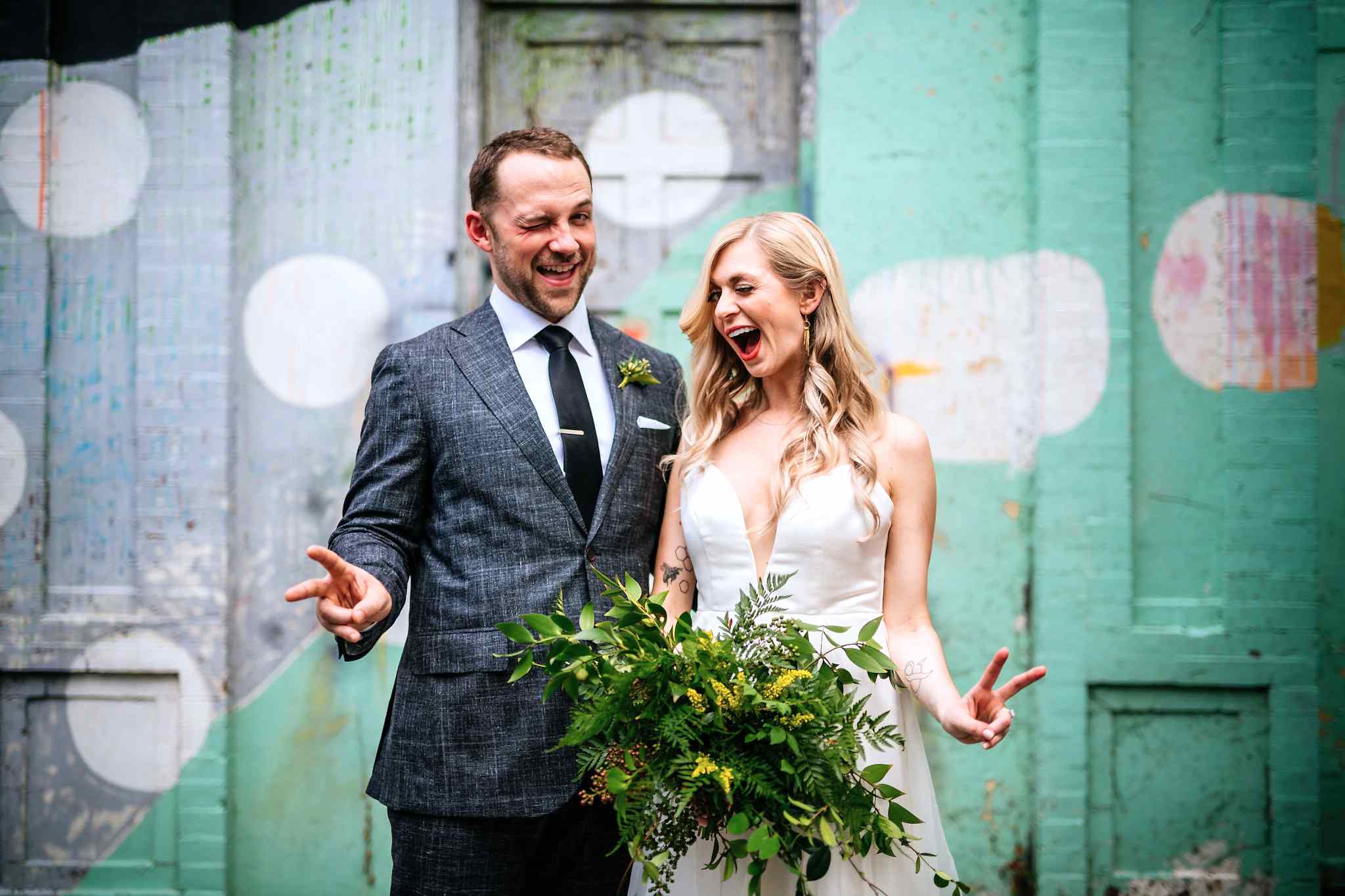 A wedding couple wink and throw up peace signs.