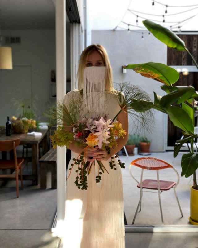 blonde woman wearing a white long fringe wedding face mask holding a bouquet