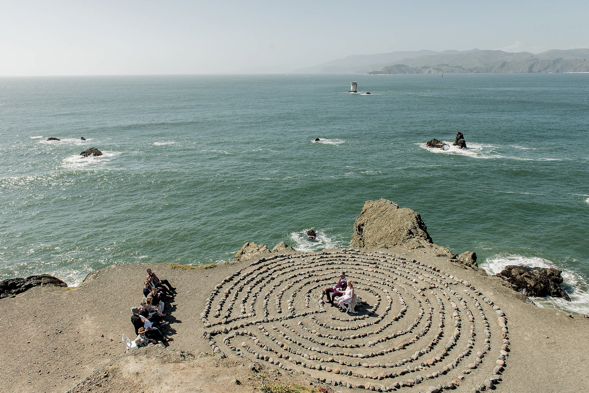 micro wedding ceremony happening in front of the ocean in a rock labrynth