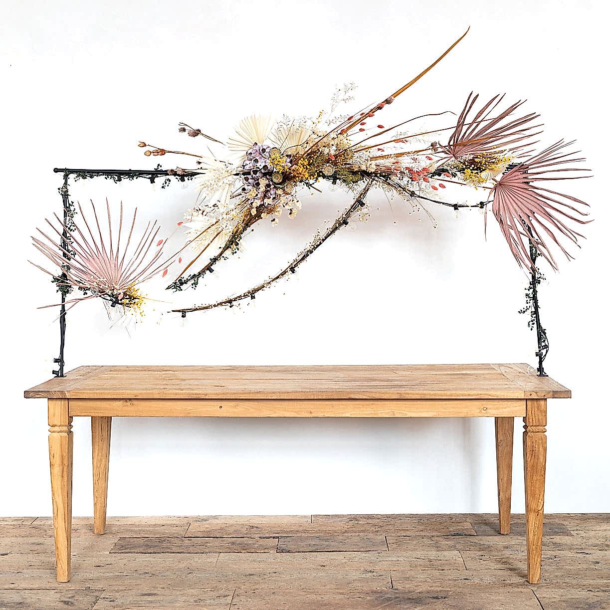 pink palm leaves and other dried flowers attached to a rod over a dinner table