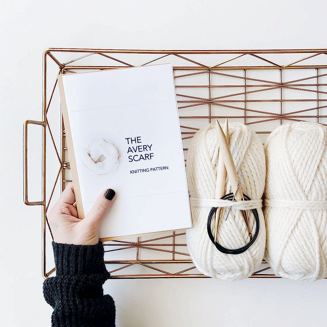 woman holding scarf knitting pattern with white yarn in basket