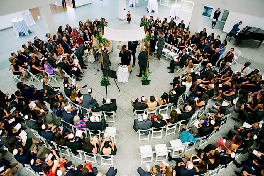 Large group of people in chairs in circle around huppah and couple during wedding ceremony