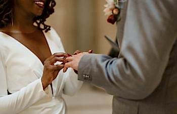 Woman in white dress placing ring on partner's finger during wedding ceremony
